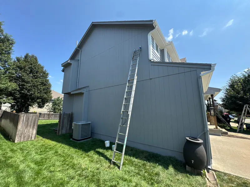 Ladder set against the freshly painted gray siding of a two-story home